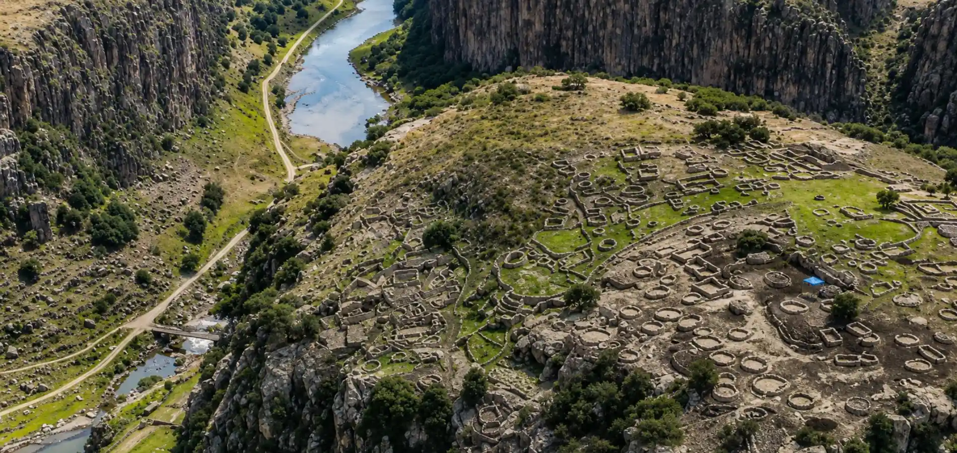 Vista aérea del Centro Arqueológico de T’aqrachullo sobre una formación rocosa junto a un río y valle andino